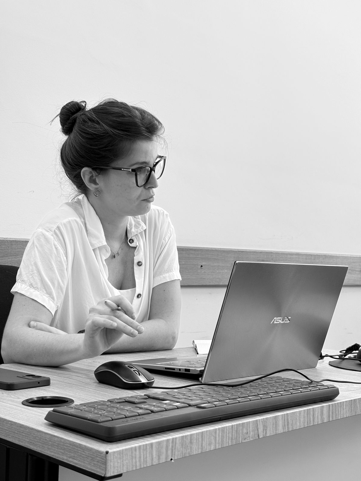 Priscilla Prada, psicanalista. Está em frente ao computador, usa óculos e veste uma camisa branca.
